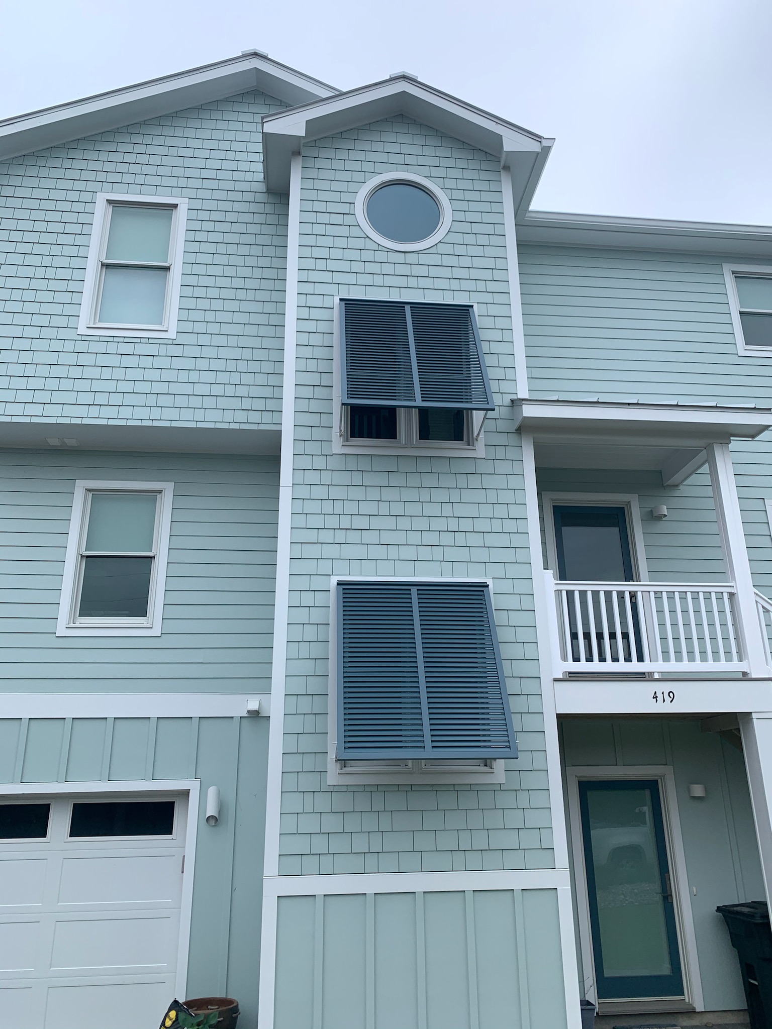 Blue house with circular and rectangular windows, some windows covered by large blue storm shutters.