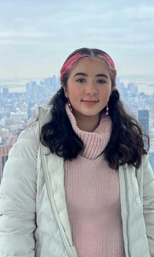 Smiling man with arms crossed, wearing a navy shirt, standing outdoors by the water.