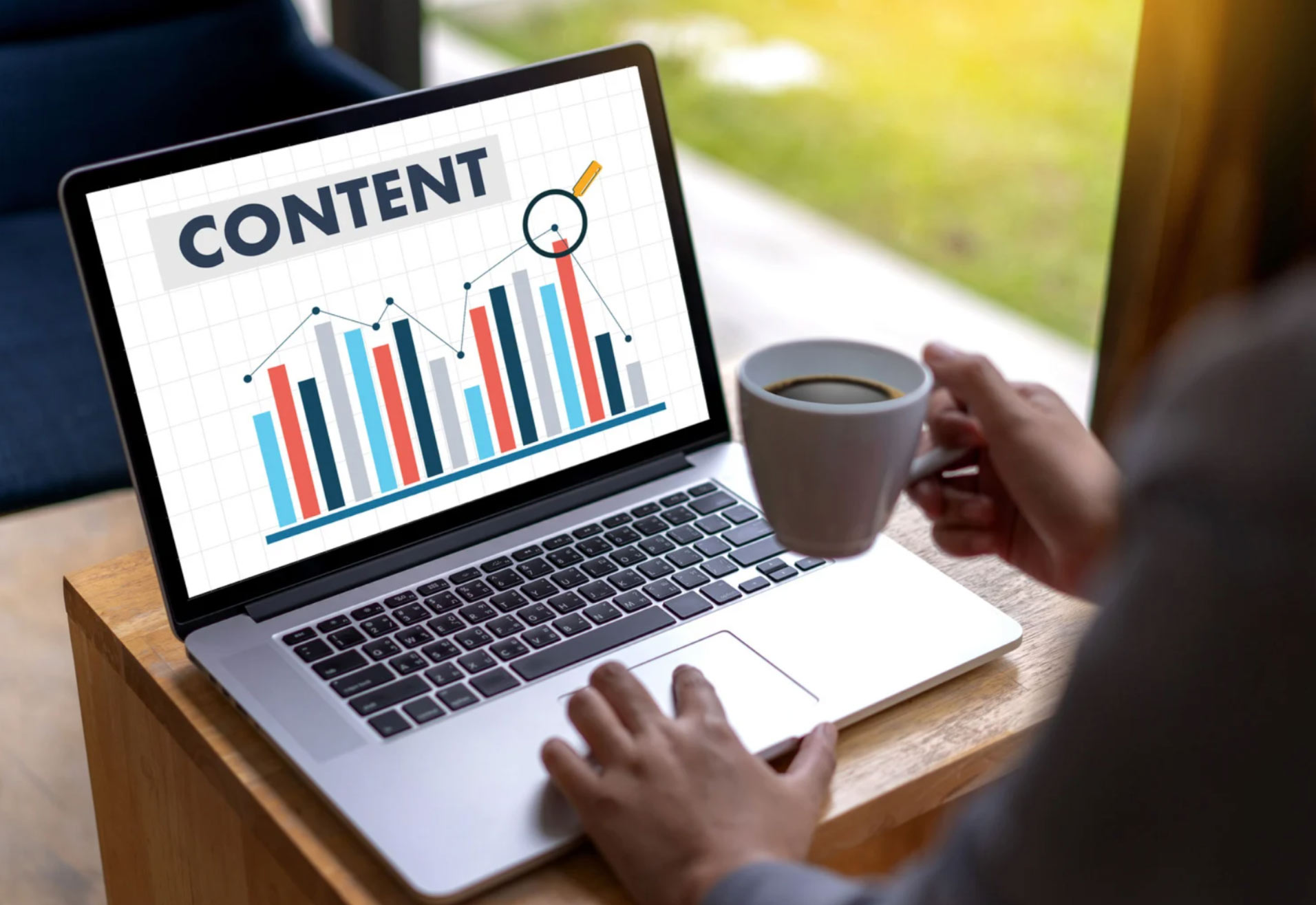 Person holding coffee cup and using laptop showing a screen with the word "CONTENT" and bar charts.