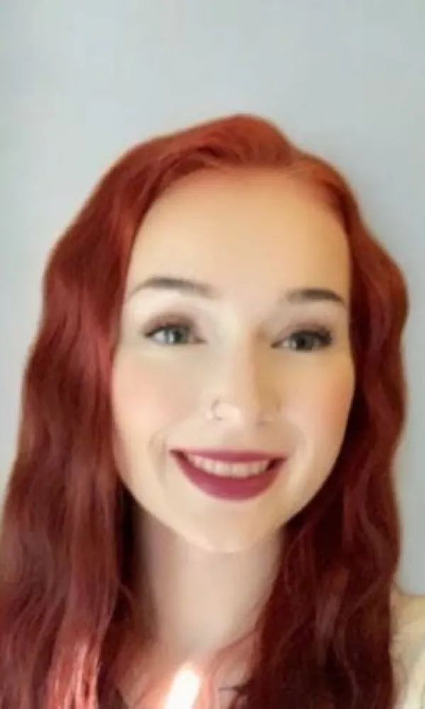 Smiling man with arms crossed, wearing a navy shirt, standing outdoors by the water.