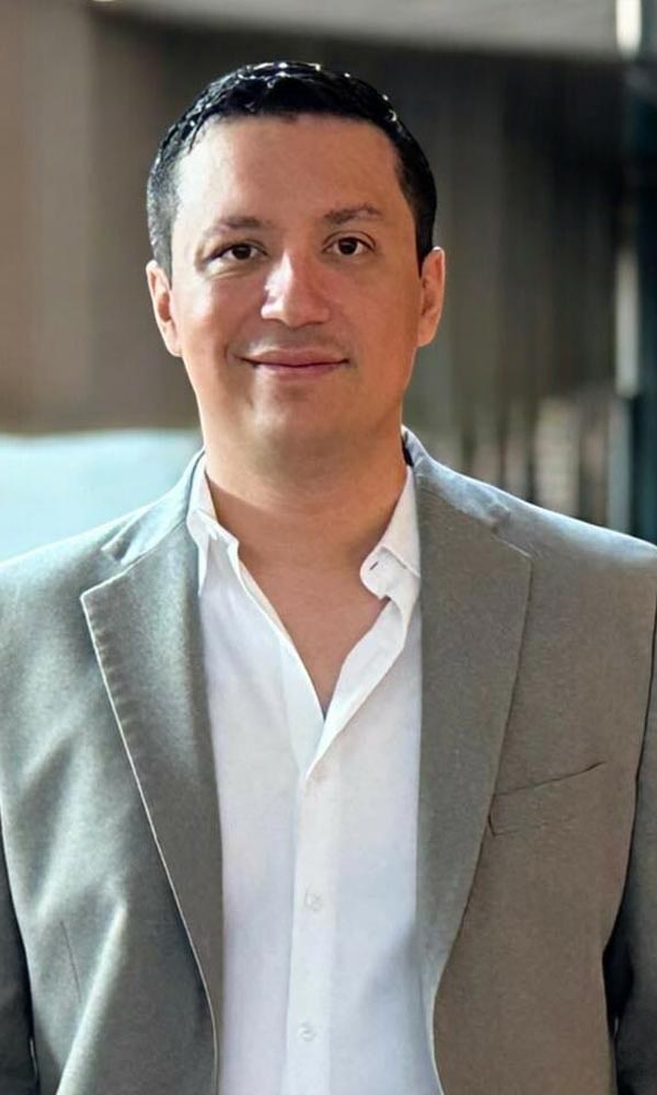 Smiling man with arms crossed, wearing a navy shirt, standing outdoors by the water.