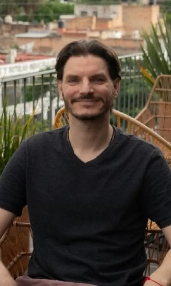 Smiling man with arms crossed, wearing a navy shirt, standing outdoors by the water.