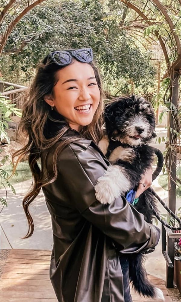 Smiling man with arms crossed, wearing a navy shirt, standing outdoors by the water.