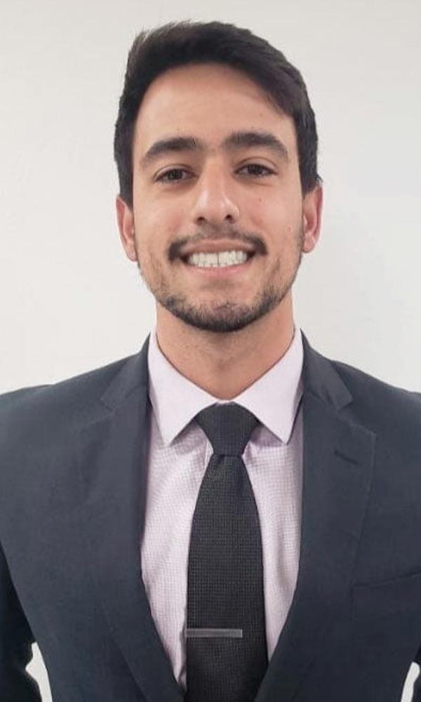 Smiling man with arms crossed, wearing a navy shirt, standing outdoors by the water.