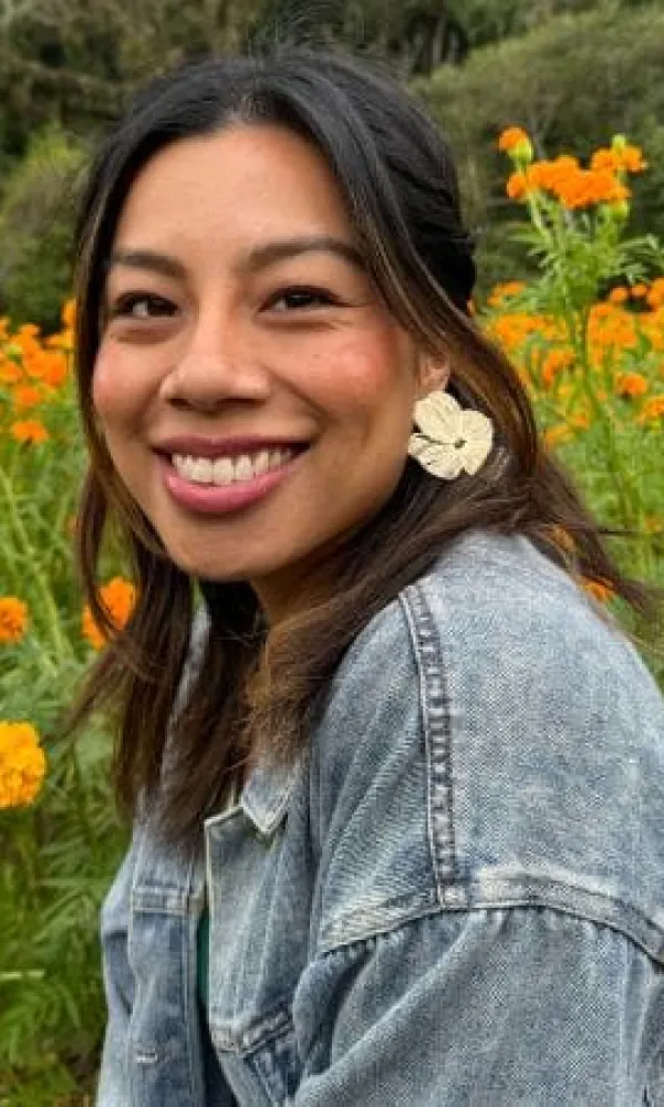 Smiling man with arms crossed, wearing a navy shirt, standing outdoors by the water.