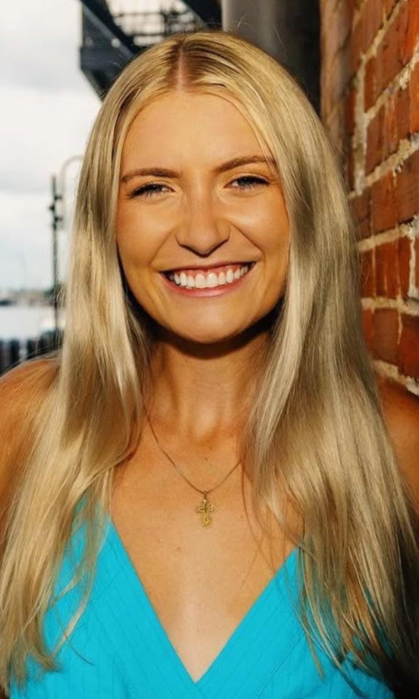 Smiling man with arms crossed, wearing a navy shirt, standing outdoors by the water.