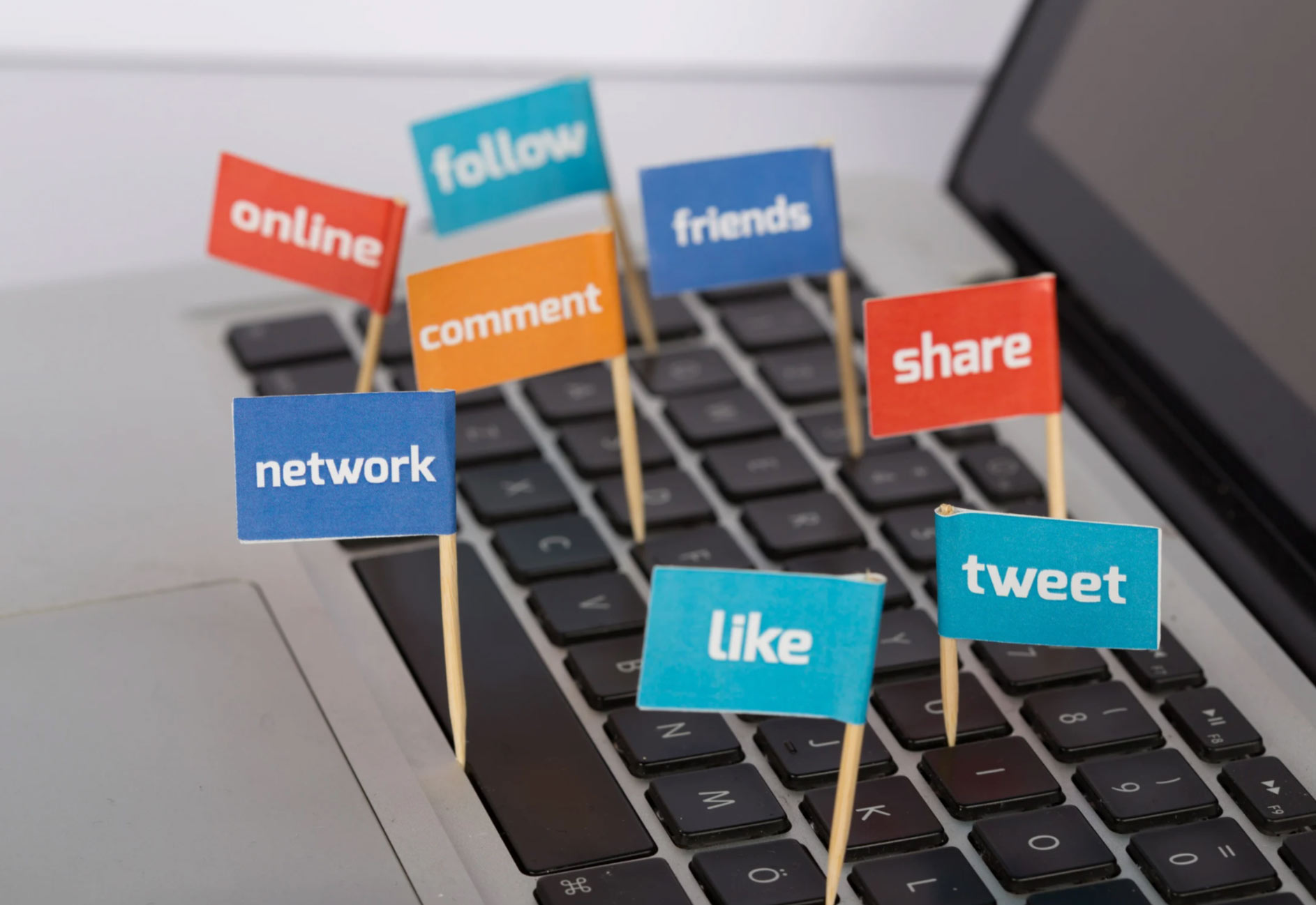 Mini signs with social media words (like, share, tweet) on sticks placed on a laptop keyboard.