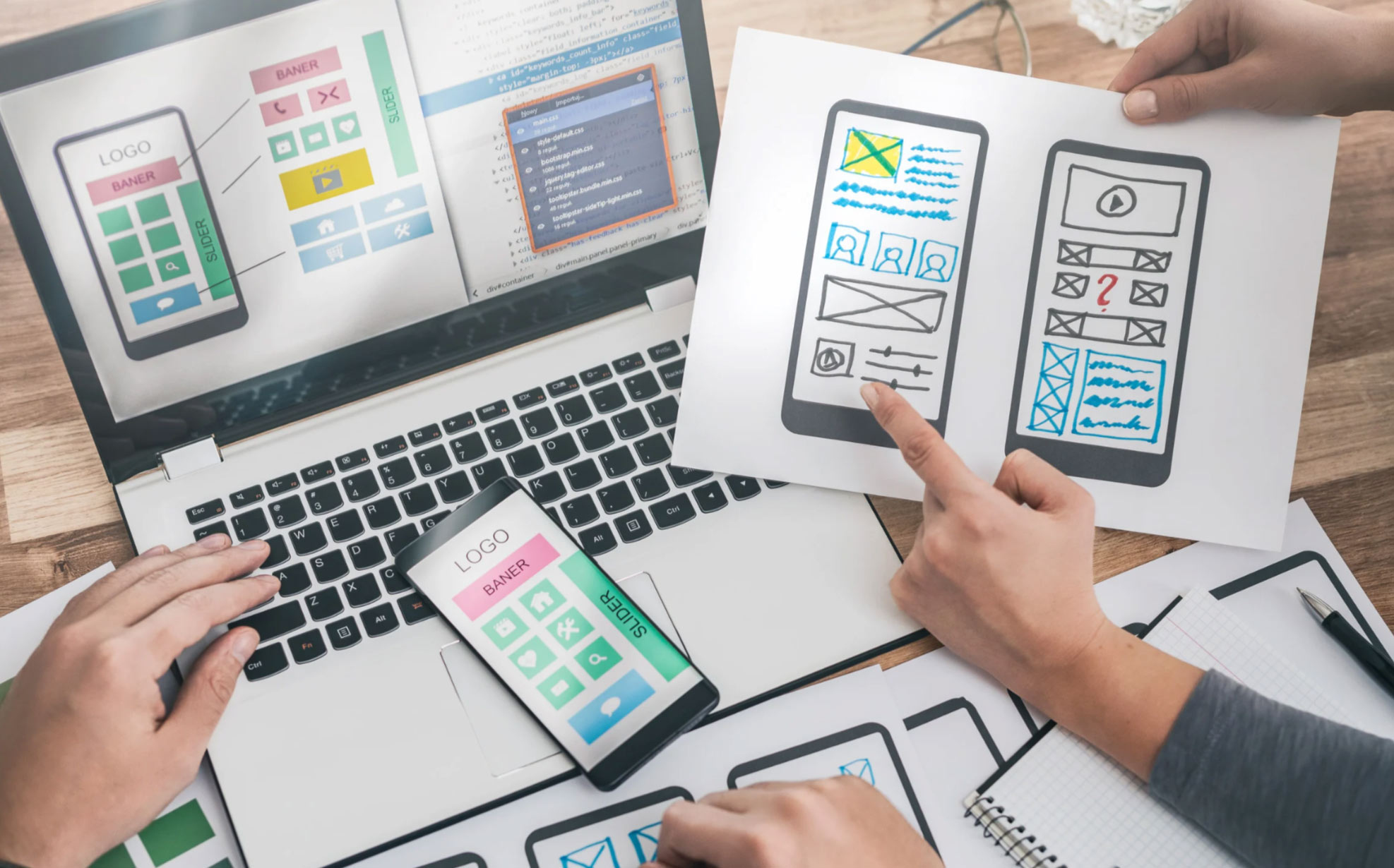 People working on mobile app wireframes with sketches, a laptop, and a smartphone on a desk.