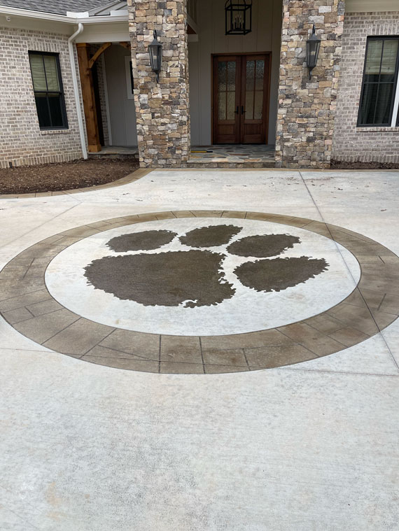 A large paw print design is stamped in the concrete driveway in front of a brick and stone house entrance.