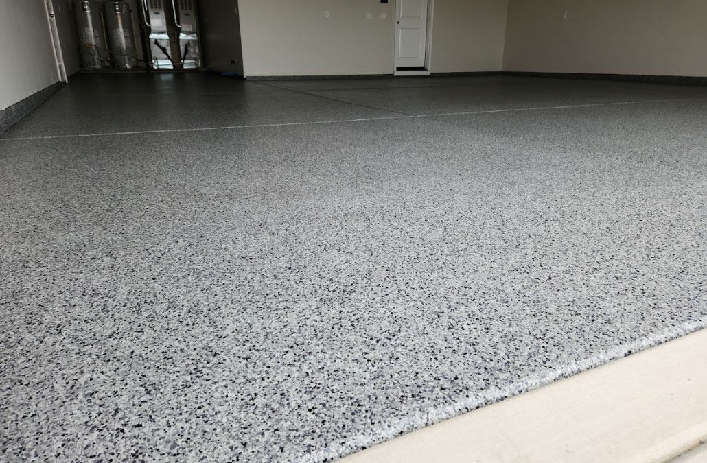 Speckled gray epoxy-coated garage floor with clean walls and closed white door in the background.