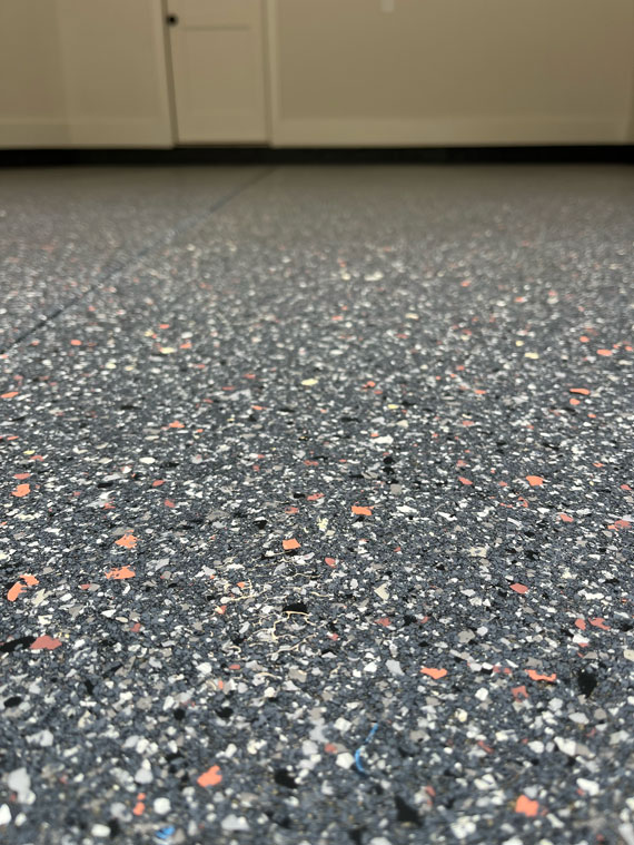 Close-up view of a speckled epoxy garage floor with a door and cabinets in the background.