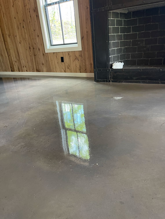 A polished concrete floor reflects a window with wood-paneled walls and a dark fireplace nearby.