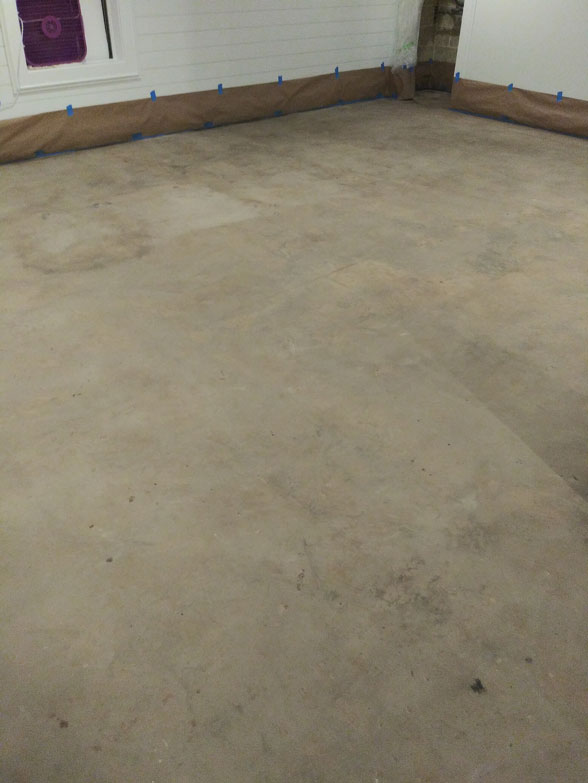 A bare concrete floor in a room with brown protective paper taped along the walls.