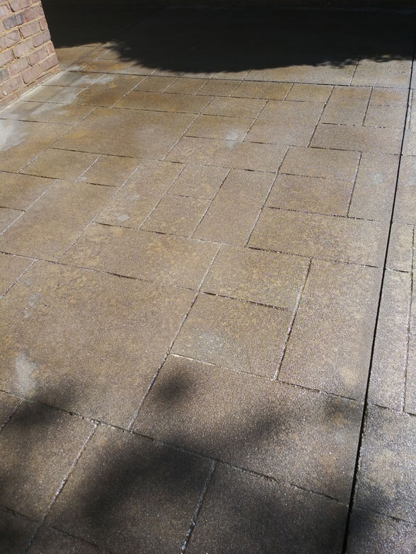 Sunlight and shadows fall across a patterned stone pavement next to a brick wall.