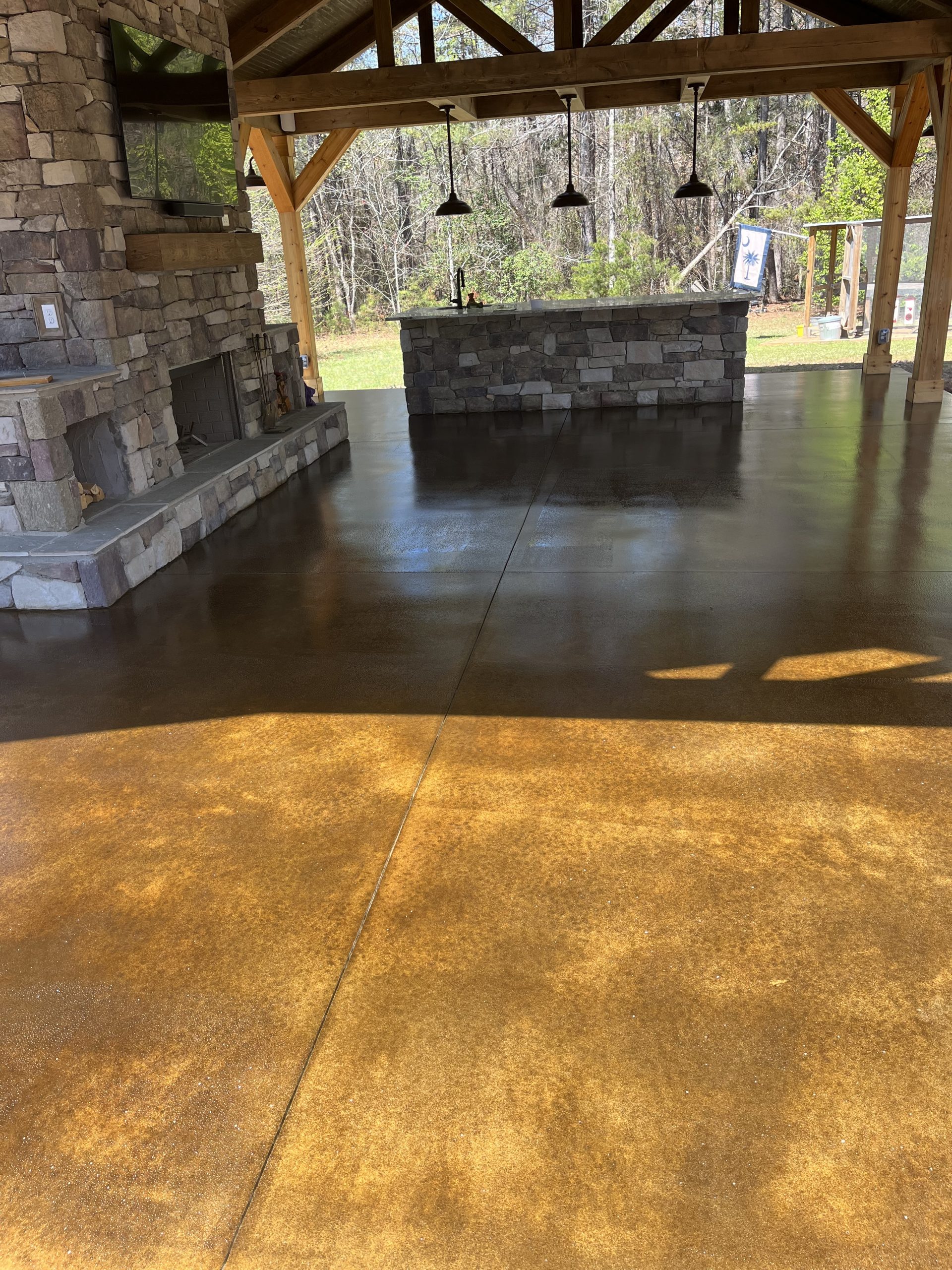Covered outdoor patio with a stone fireplace, bar area, and polished brown concrete floor.