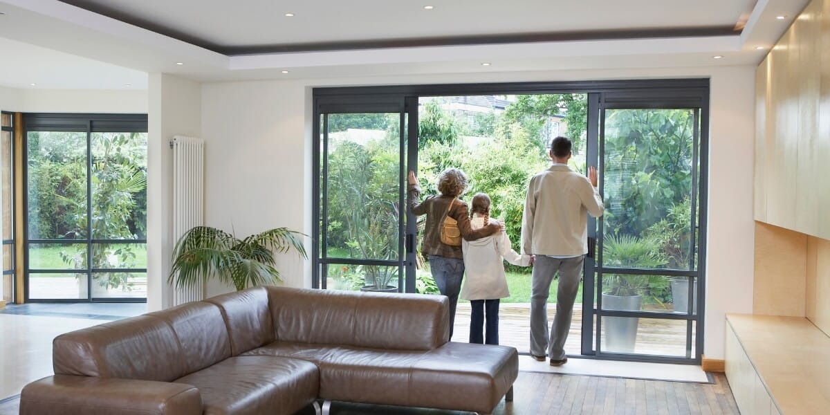 Rear view of parents and daughter looking out opened sliding glass door in a sleek, modern home with clean lines and biophilic design.