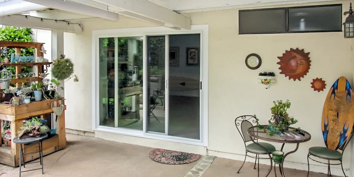 Patio with sliding patio doors, small table and chairs, plant shelf, and wall decor including a sun and surfboard. Patio with sliding patio doors, small table and chairs, plant shelf, and wall decor including a sun and surfboard.